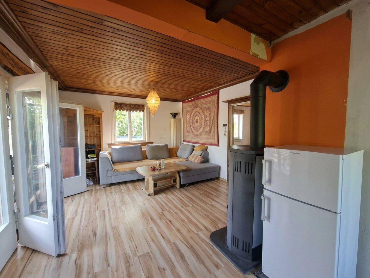 Gemütliches Wohnzimmer mit Kaminofen, Holzdecke und Zugang zur Terrasse.