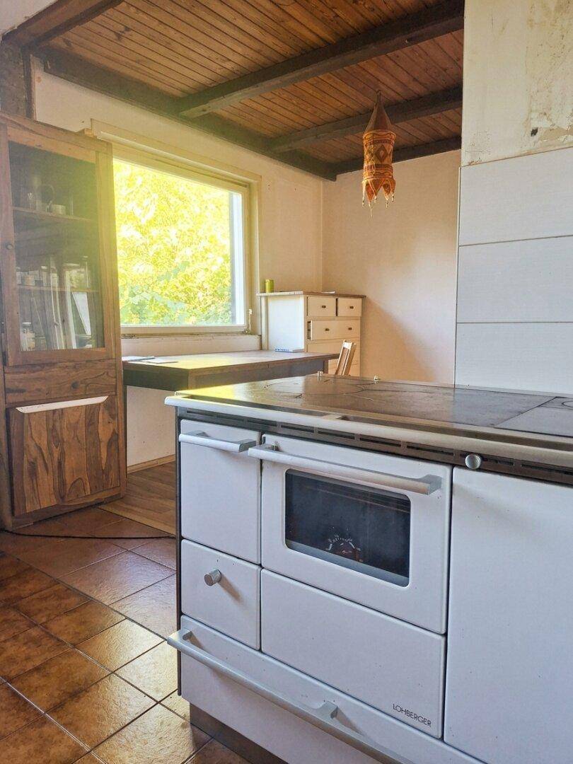 Traditionelle Küche mit Holzofen, Fliesenboden und Fenster mit Blick ins Grüne.