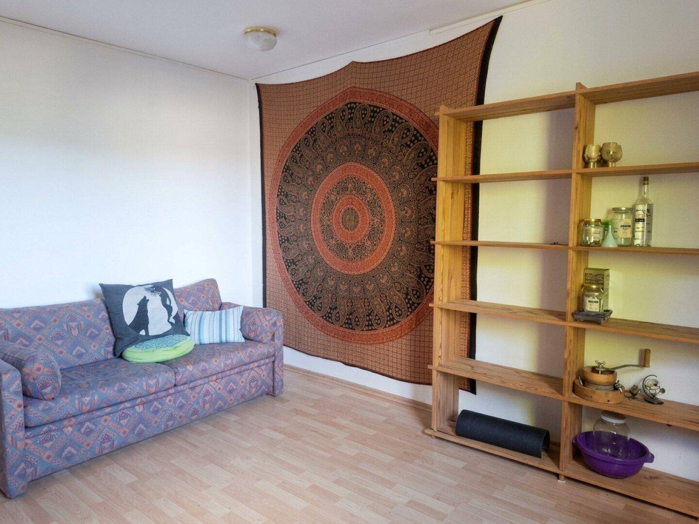 Einfacher Wohnraum mit Sofa, Holzregal und dekorativem Wandteppich.