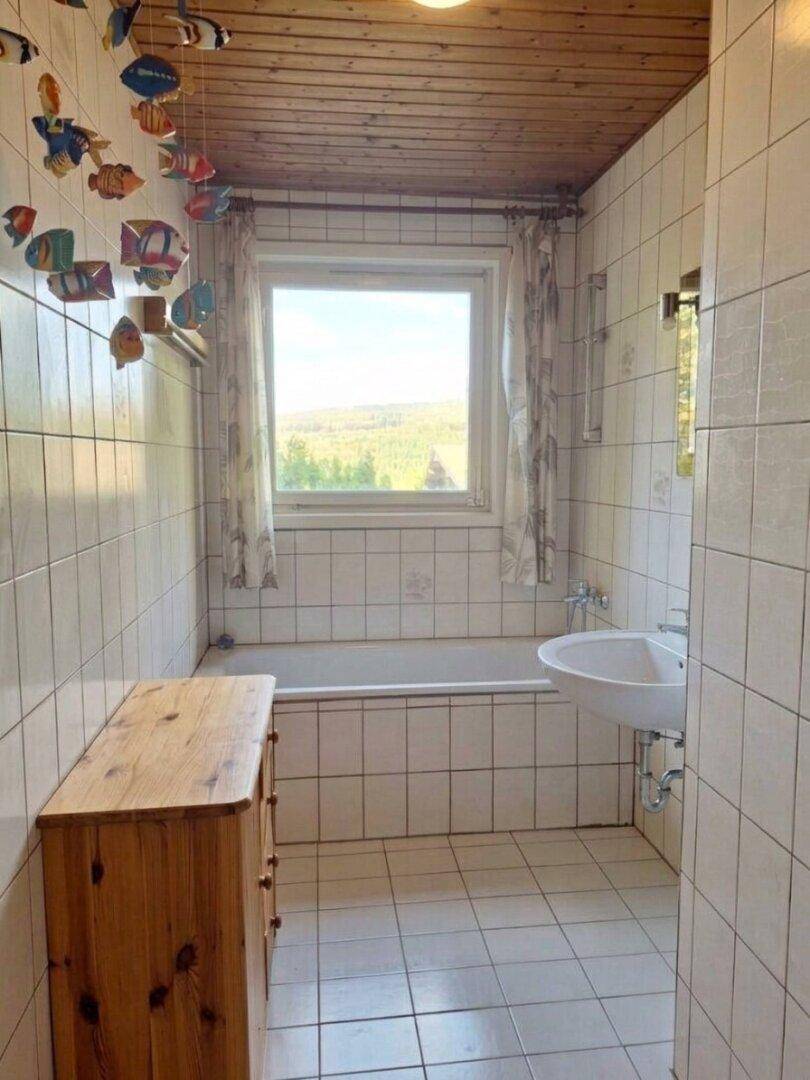 Gefliestes Badezimmer mit Badewanne, Waschbecken und Fenster mit Fernblick.