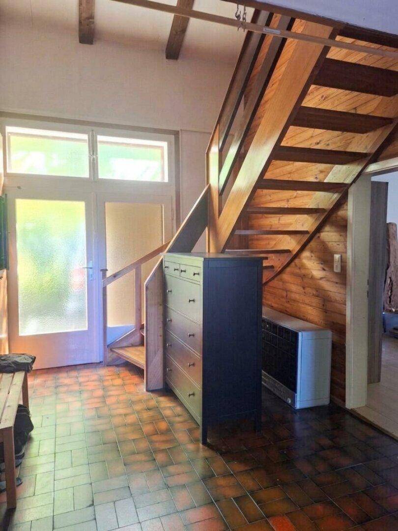 Eingangsbereich mit Holztreppe, Fliesenboden und natürlichem Lichteinfall.