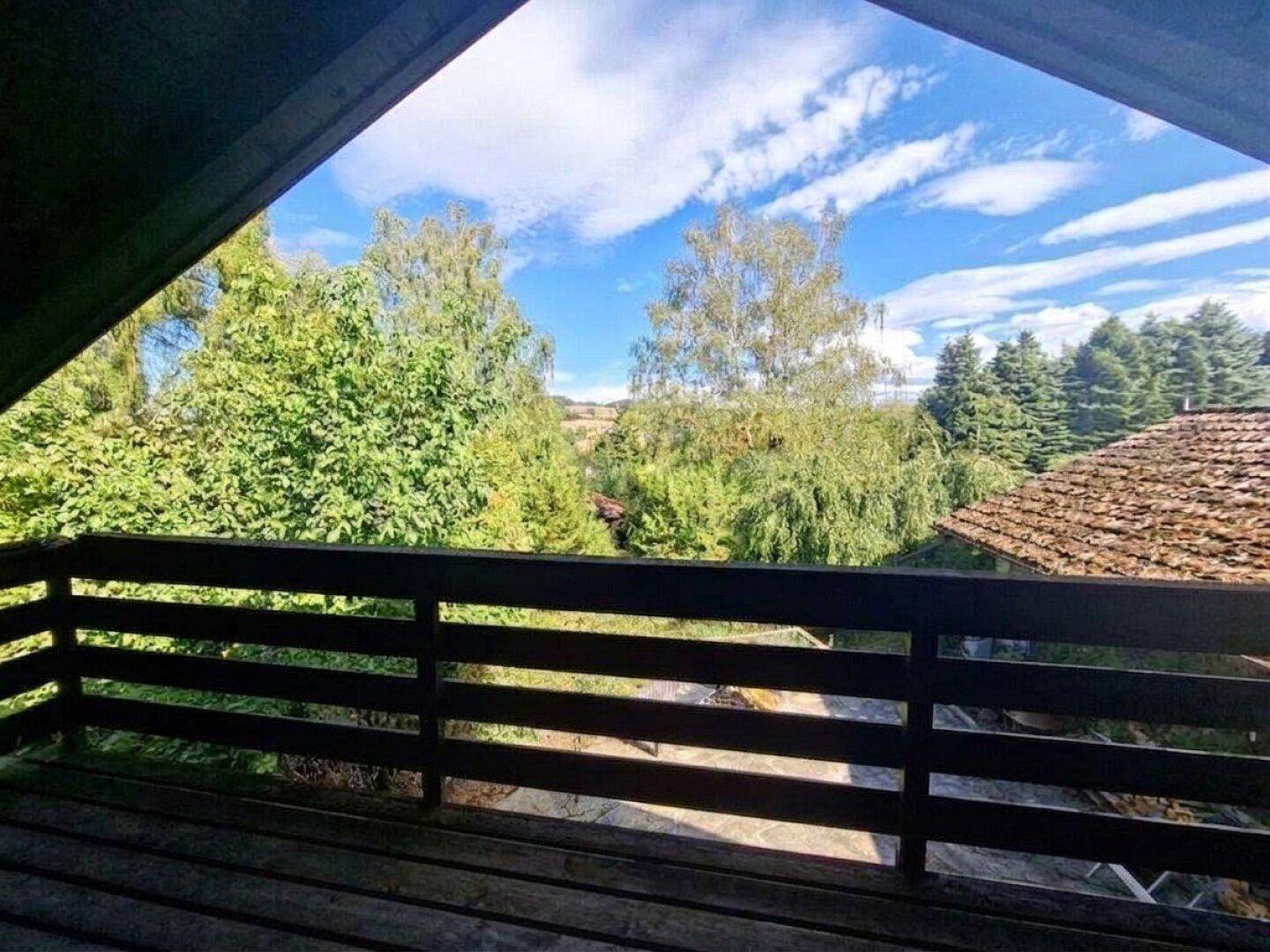Balkon mit Holzboden und weitem Blick über die grüne Landschaft und Dächer.