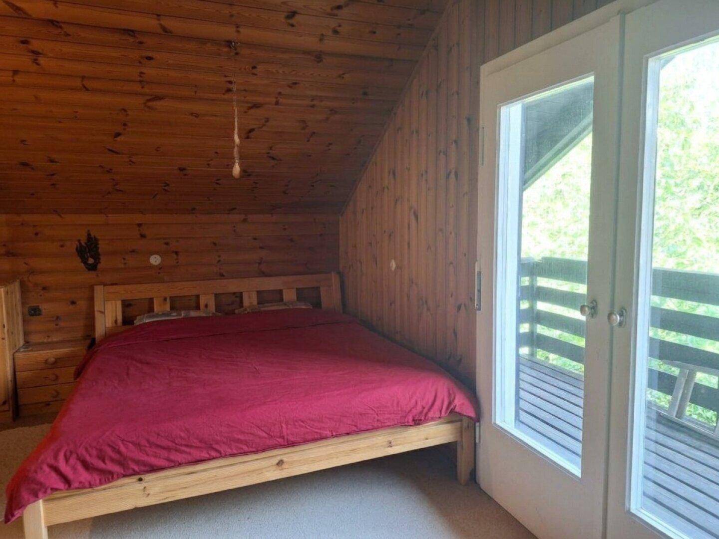 Schlafzimmer mit Holzwänden, Doppelbett und direktem Zugang zum Balkon.
