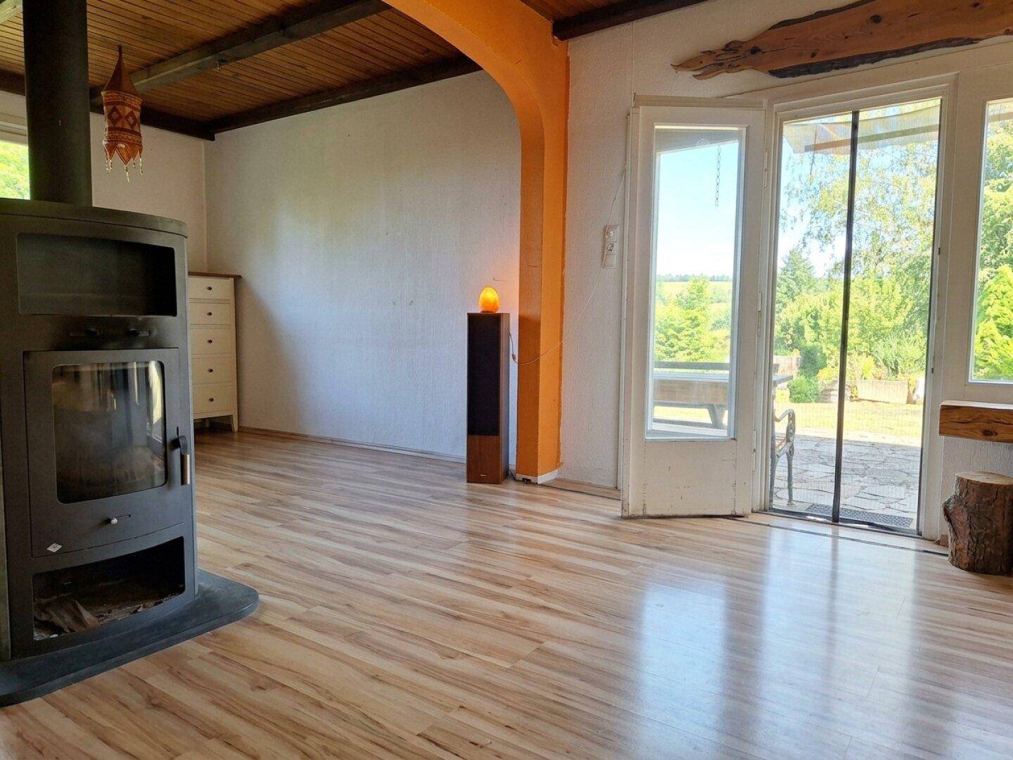 Helles Wohnzimmer mit Kaminofen, Holzboden und weitem Blick in die Landschaft.