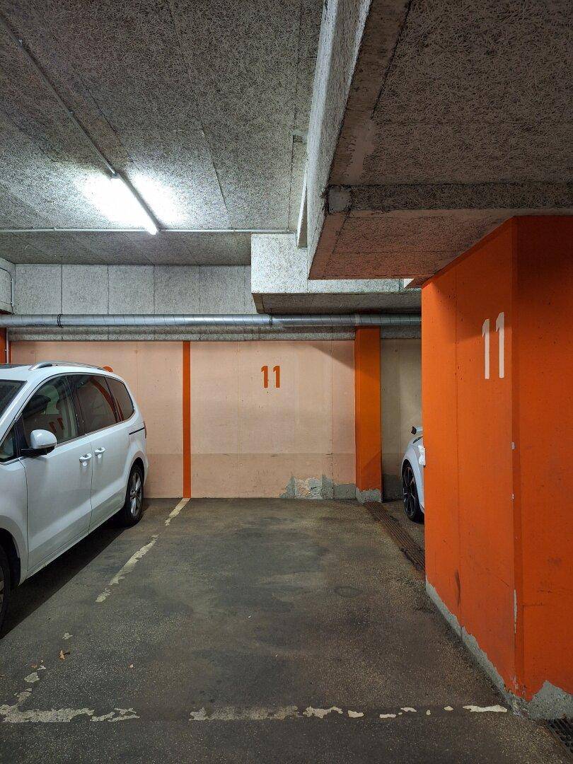 Tiefgarage mit nummerierten Parkplätzen, orangefarbenen Säulen und geparkten Fahrzeugen.
