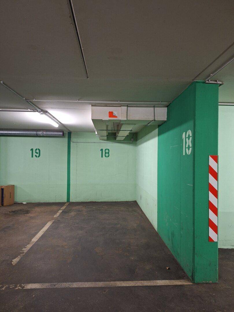 Tiefgarage mit grünen Wänden und Säulen, nummerierten Parkplätzen und Betonboden.