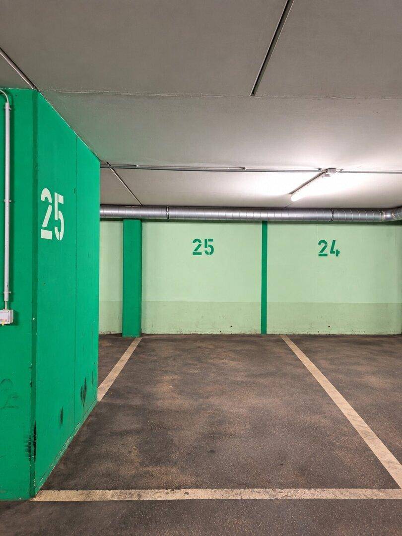 Tiefgarage mit hellgrünen Wänden, nummerierten Parkplätzen und sichtbaren Lüftungsrohren.