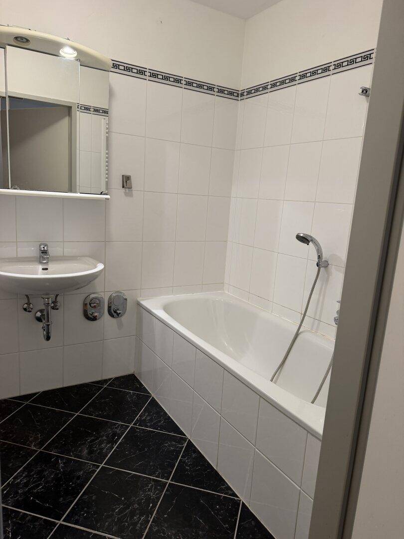 Badezimmer mit Badewanne, Waschbecken und schwarz-weiß gefliestem Boden und Wänden.