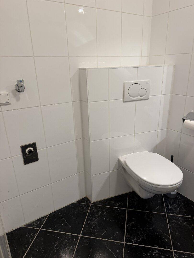 Wand-WC in einem gefliesten Badezimmer mit modernem Spülkasten.