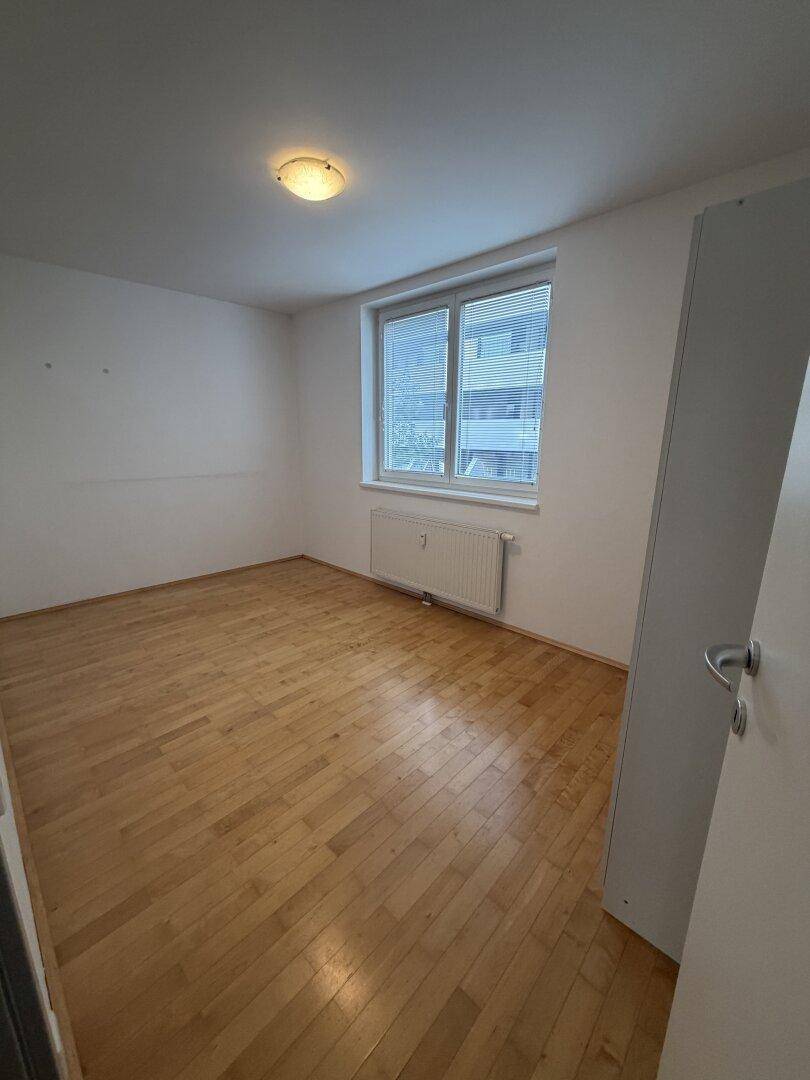 Leeres Schlafzimmer mit Parkettboden, Fenster und Heizkörper.