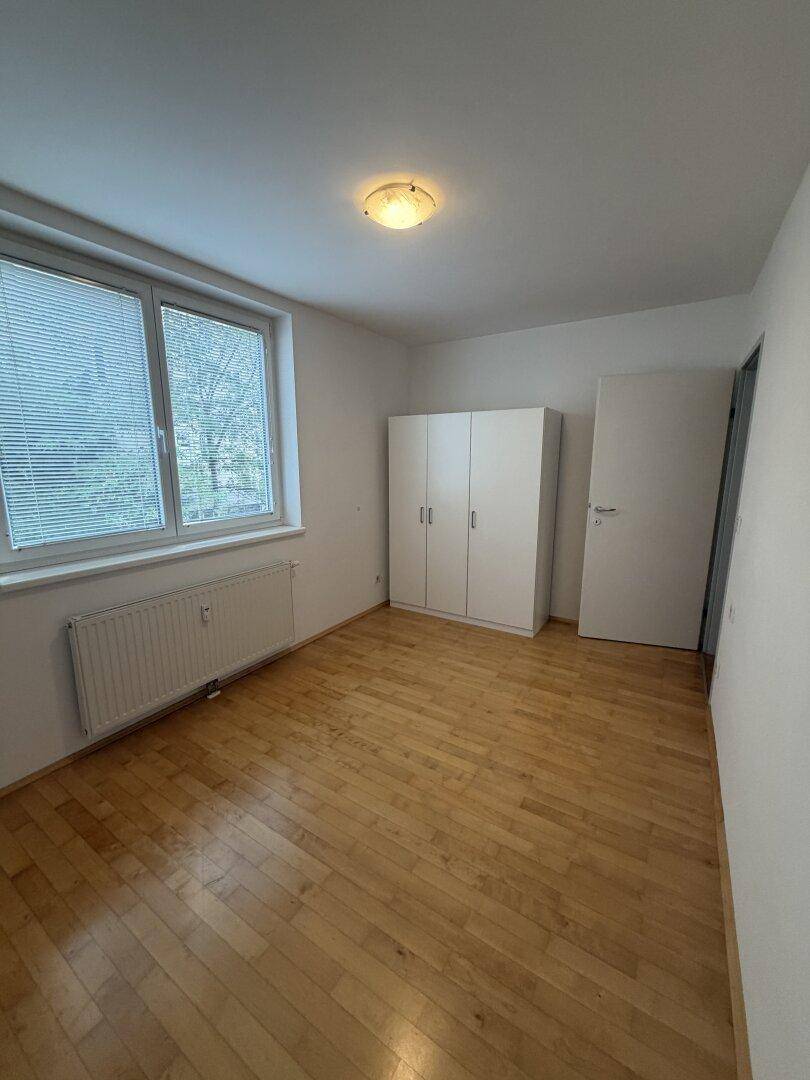 Helles Schlafzimmer mit Parkettboden, Fenster und einem weißen Kleiderschrank.