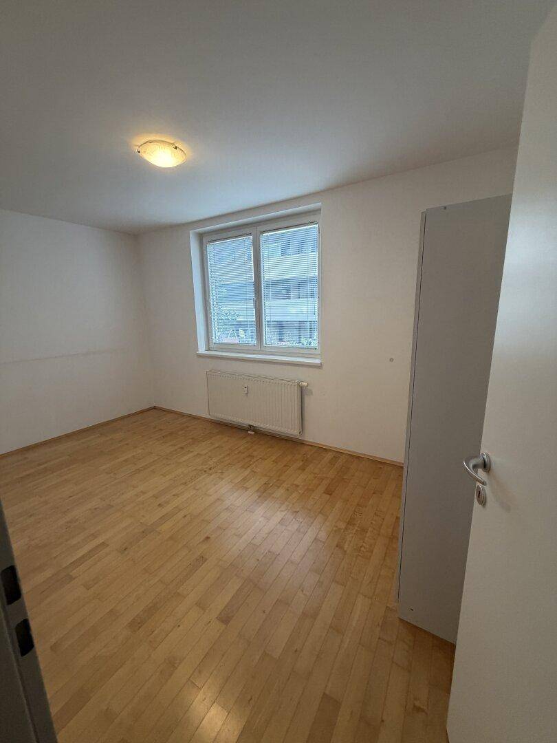 Leeres Schlafzimmer mit Parkettboden und Fenster, bereit zur Einrichtung.