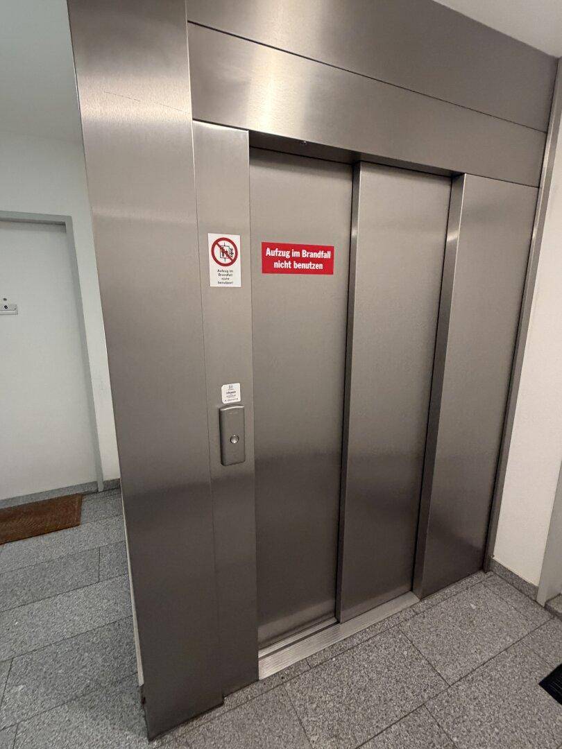 Moderner Aufzug im Gebäude mit Edelstahloberfläche und Hinweisschildern.