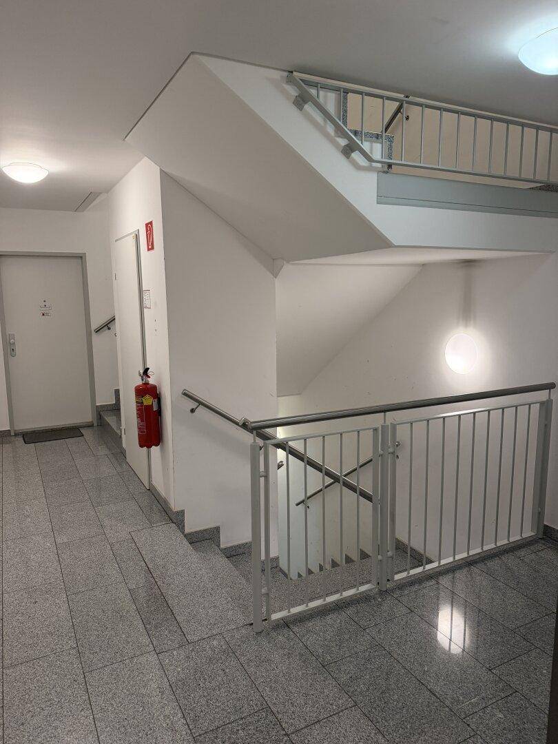 Treppenhaus mit Fliesenboden, Geländer und Feuerlöscher.