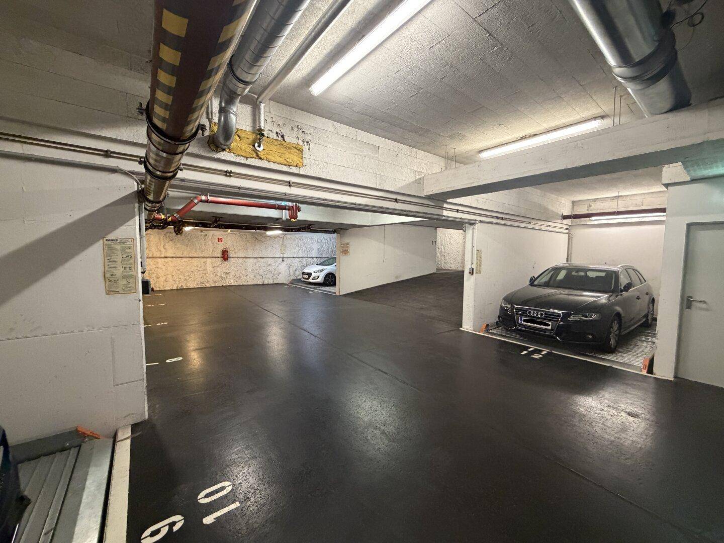Tiefgarage mit mehreren Stellplätzen und sichtbaren Leitungen an der Decke.