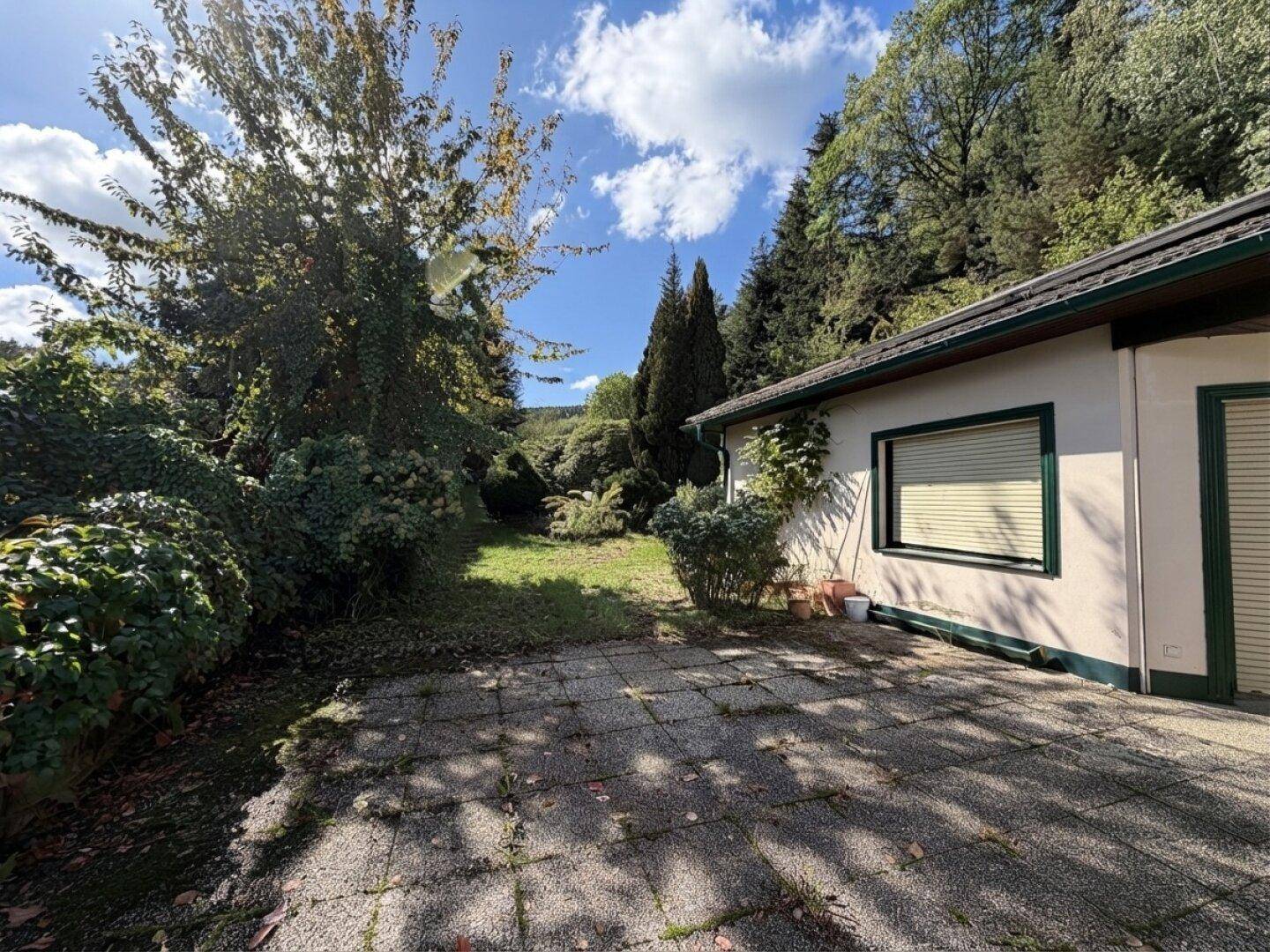Seitliche Terrasse mit Steinplatten und Blick auf den grünen Gartenbereich.