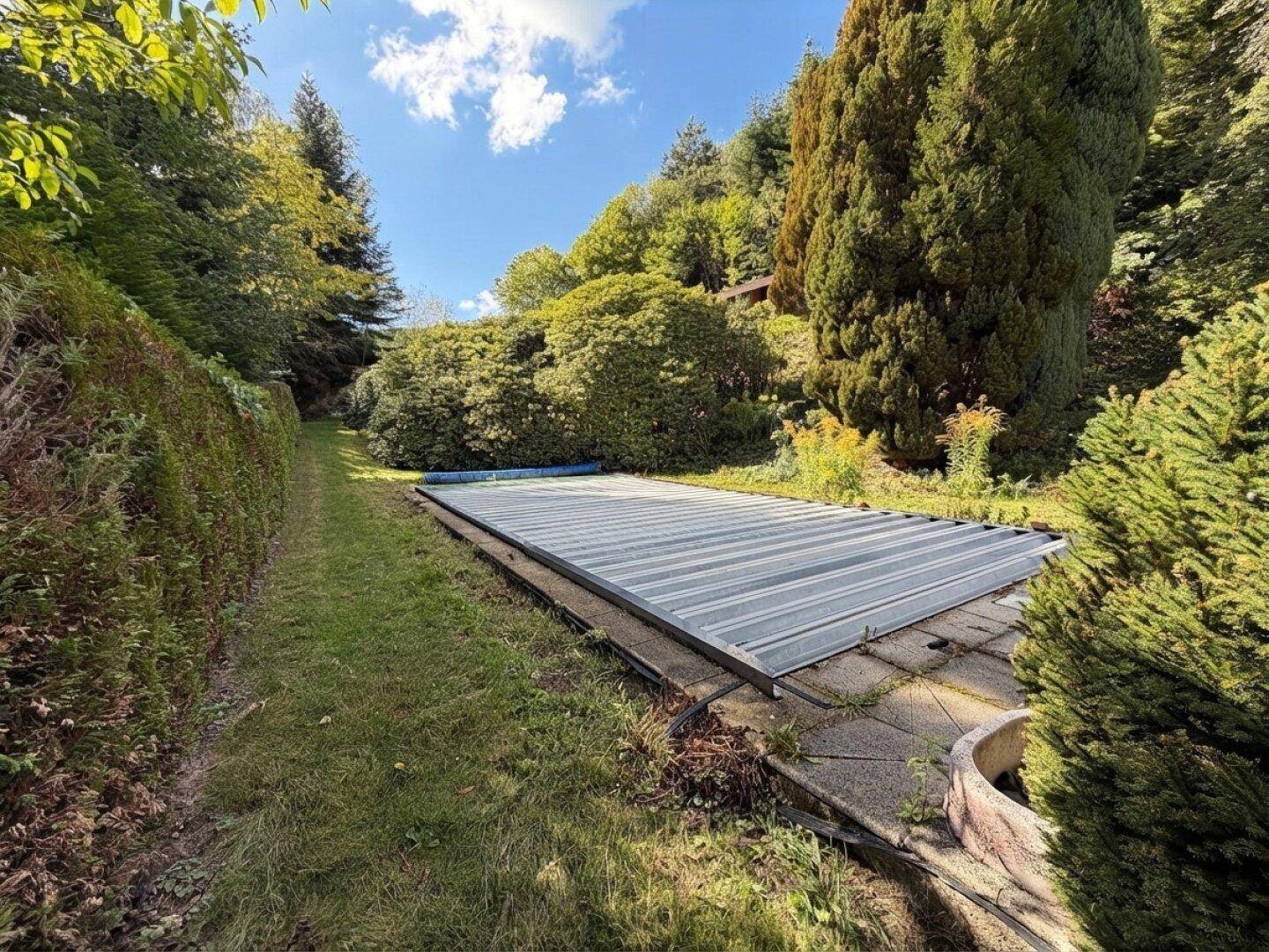 Großer Gartenbereich mit abgedecktem Pool, umgeben von hohen Hecken und Bäumen.