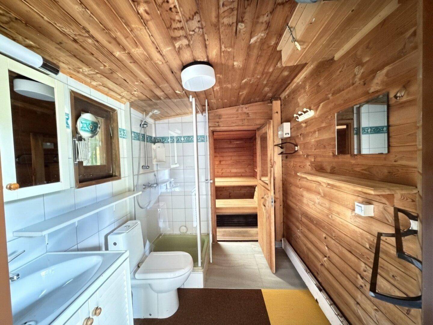 Badezimmer mit Dusche, Waschbecken und integrierter Sauna, holzvertäfelte Wände.