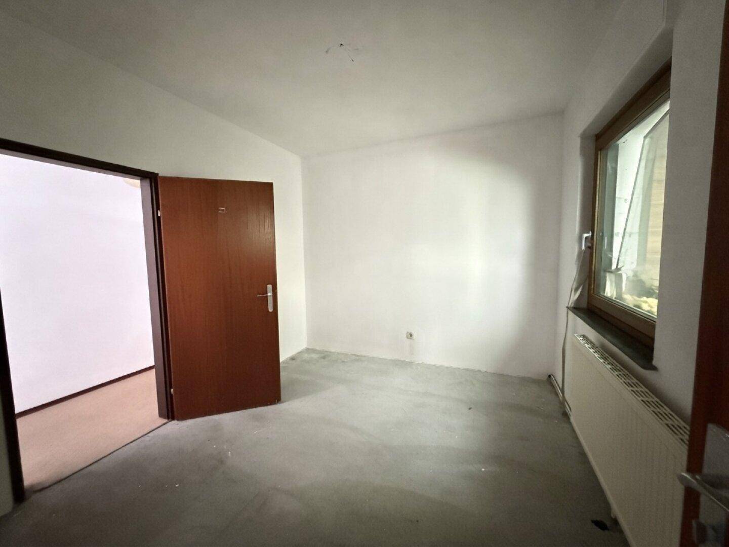 Leeres Zimmer mit hellen Wänden und einfachem Bodenbelag, bereit zur individuellen Gestaltung.