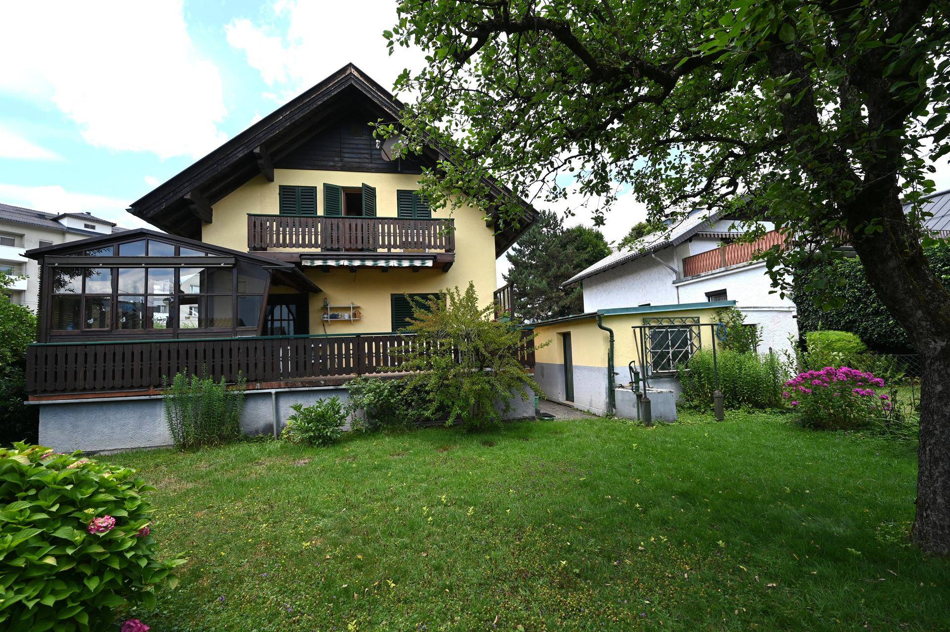 Großer, gepflegter Garten hinter dem Haus mit Rasenfläche, Bäumen und Wintergarten.