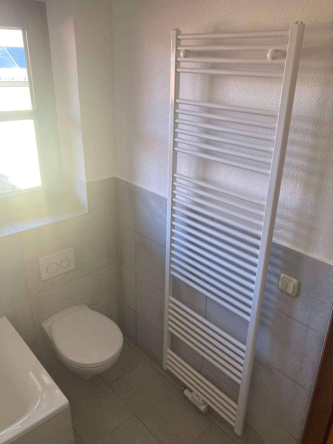 Badezimmer mit WC, beheiztem Handtuchhalter und Fenster für Tageslicht.