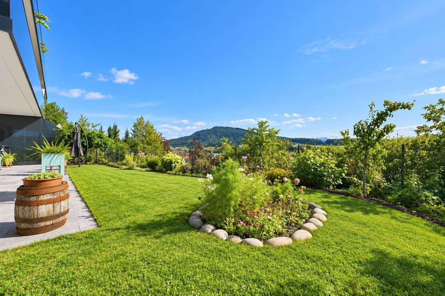 Gepflegter Garten mit Rasenfläche, Blumenbeeten und einem malerischen Blick auf die umliegende Hügellandschaft.