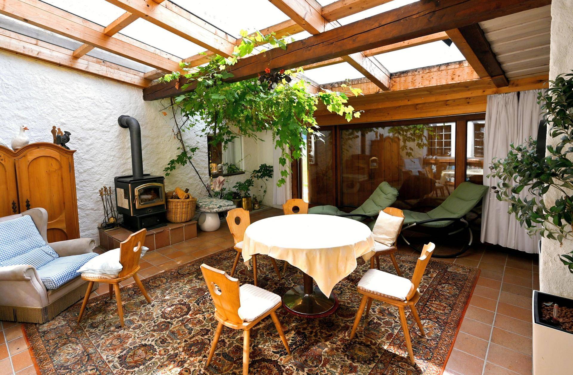 Gemütlicher Wintergarten mit Holzdachkonstruktion, Kaminofen und üppiger Bepflanzung.