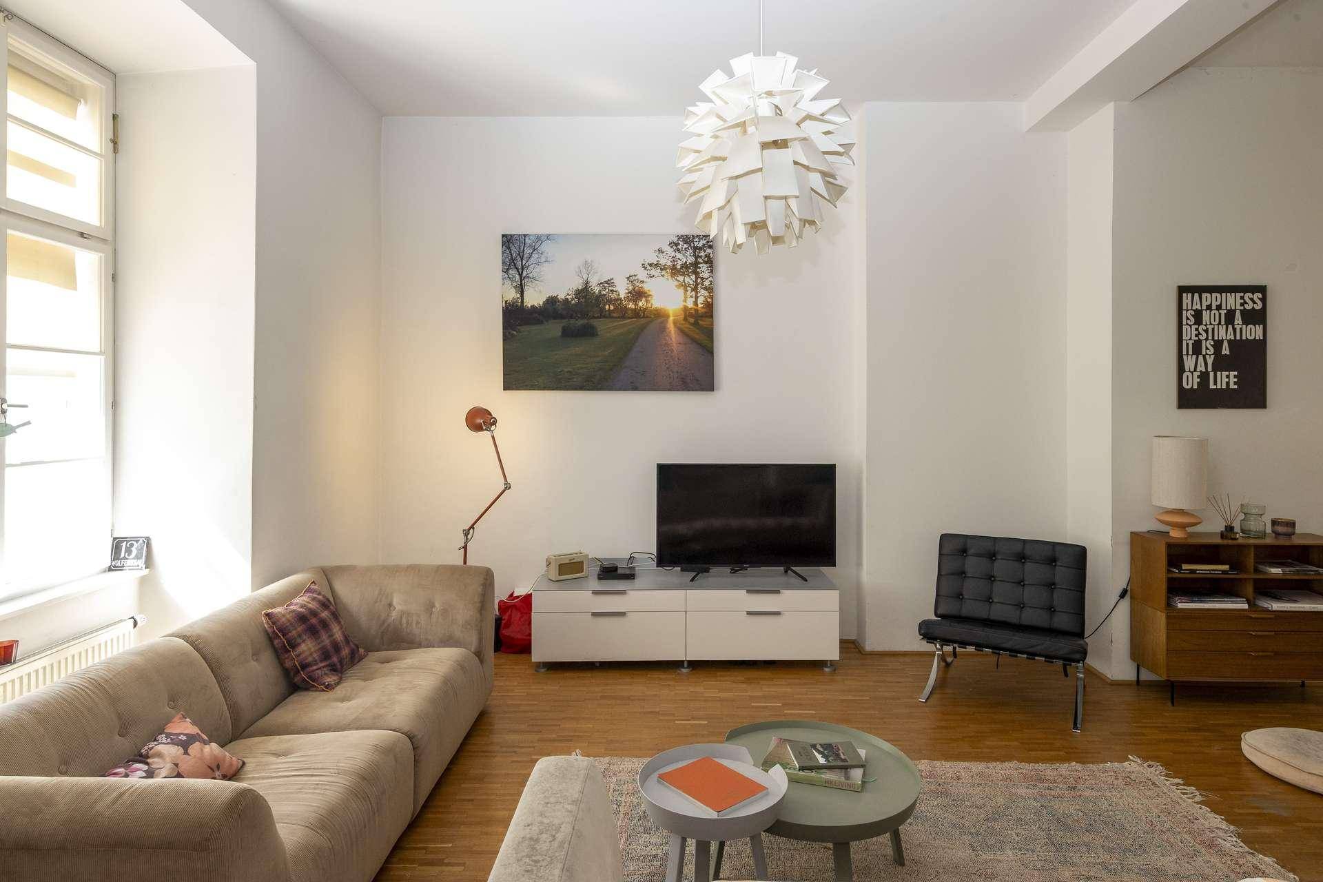 Helles Wohnzimmer mit beigem Sofa, Fernseher und stilvoller Dekoration, ergänzt durch Holzboden.
