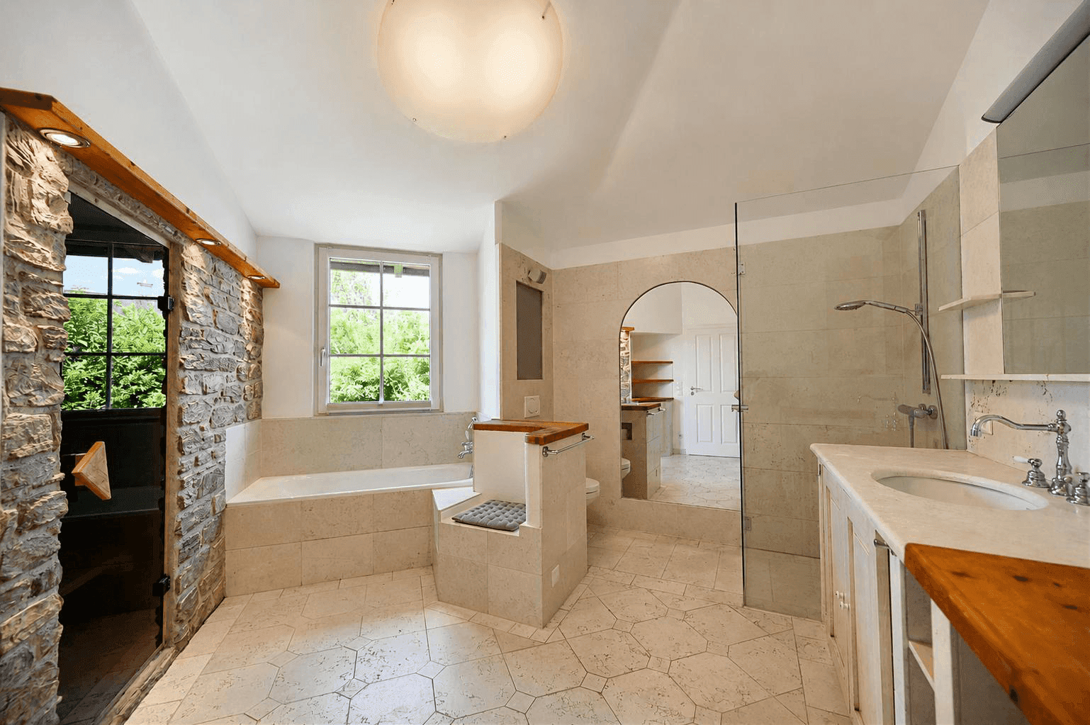 Großzügiges Badezimmer mit Sauna, Badewanne, begehbarer Dusche und Steinwandakzenten.