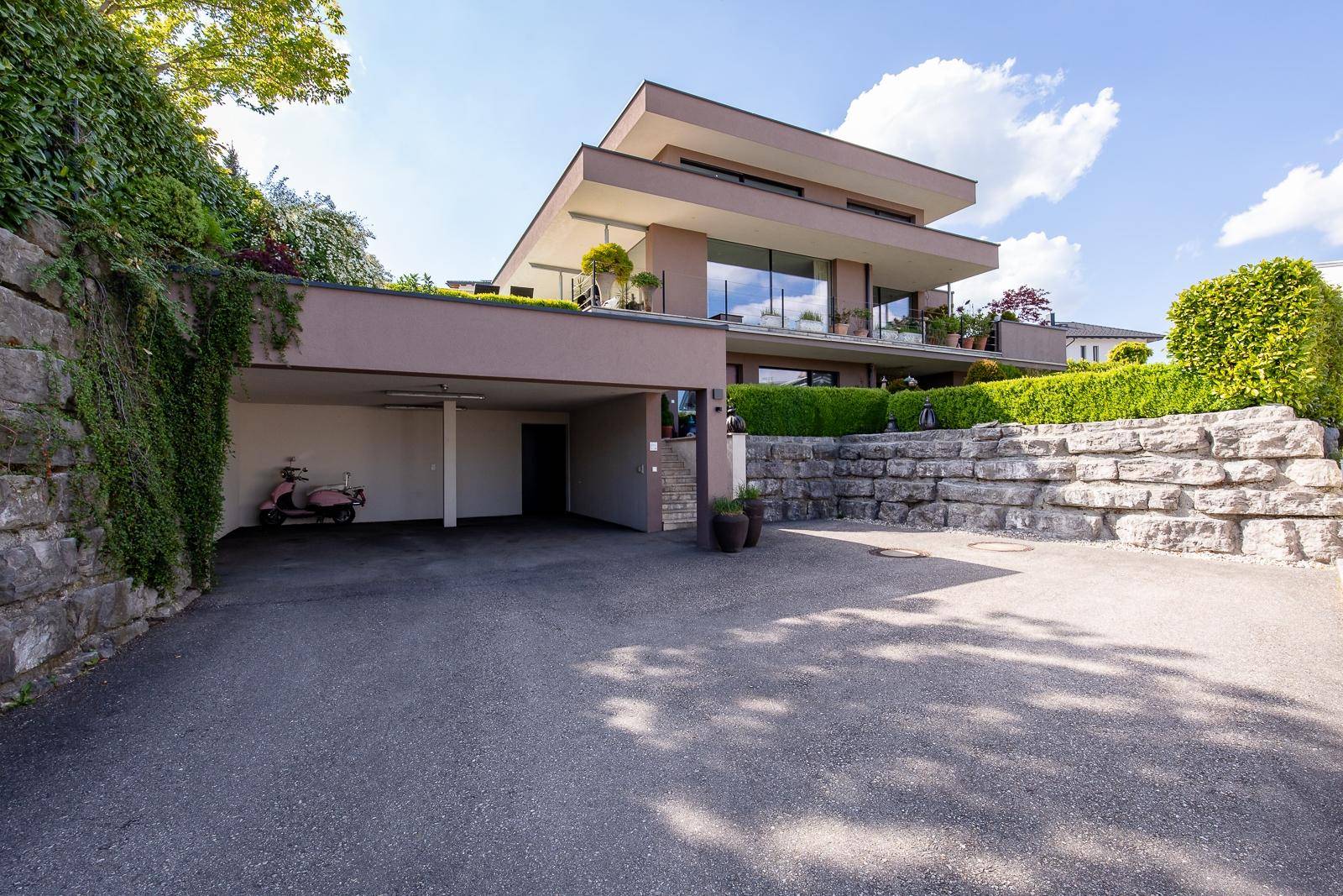 Moderne Villa mit großzügiger Architektur, Carport und gepflegter Außenanlage mit Steinmauern.
