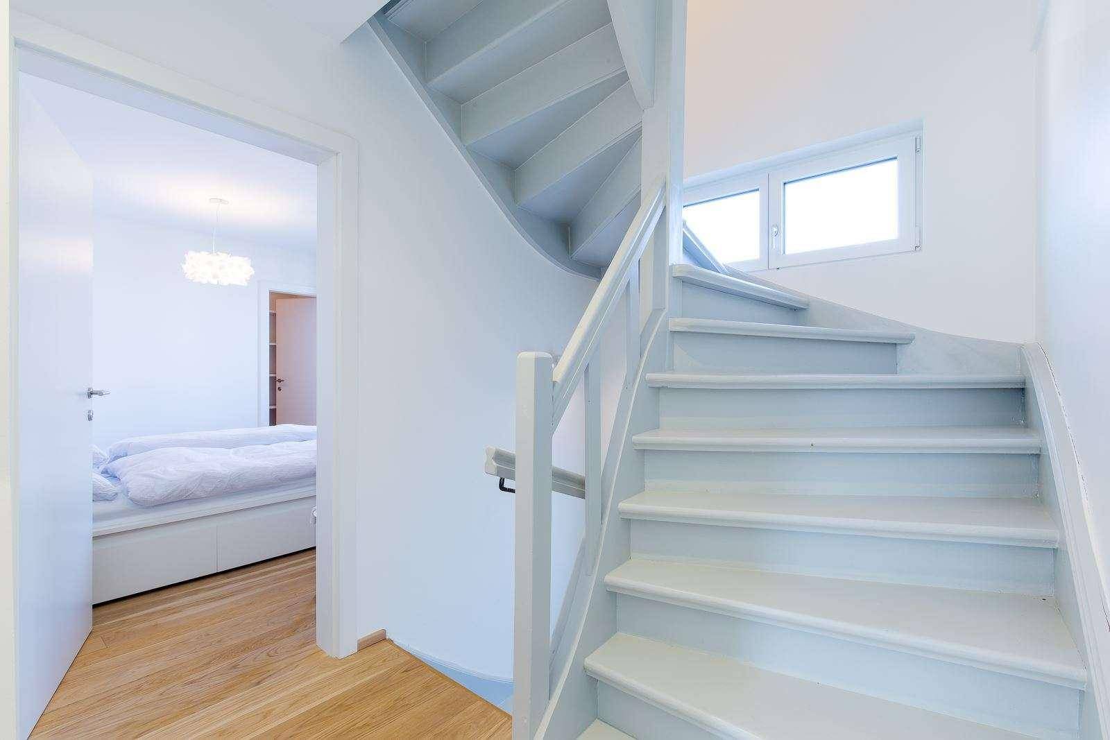 Helle Holztreppe führt in die obere Etage, mit Fenster und Blick ins Schlafzimmer.