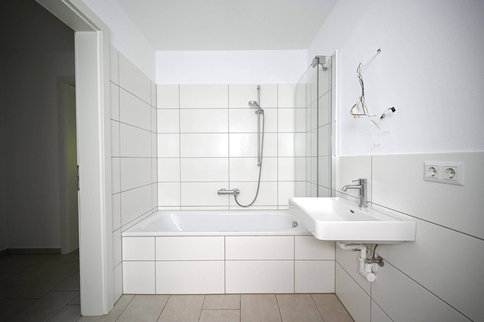 Modernes Badezimmer mit weißen Fliesen, Badewanne mit Duschwand und einem Waschbecken.