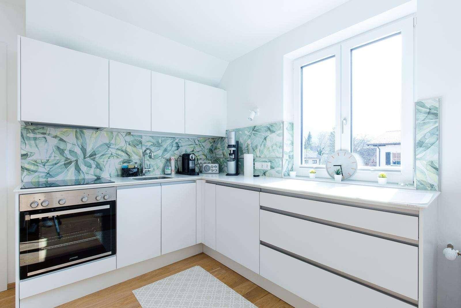 Funktionale weiße Küche mit integriertem Backofen, Spüle und Fenster für Tageslicht.