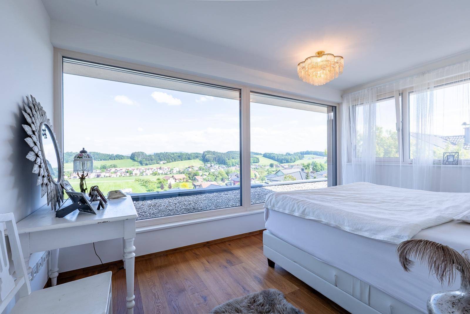 Schlafzimmer mit Panoramafenstern, Holzboden und weitem Blick über die Landschaft.