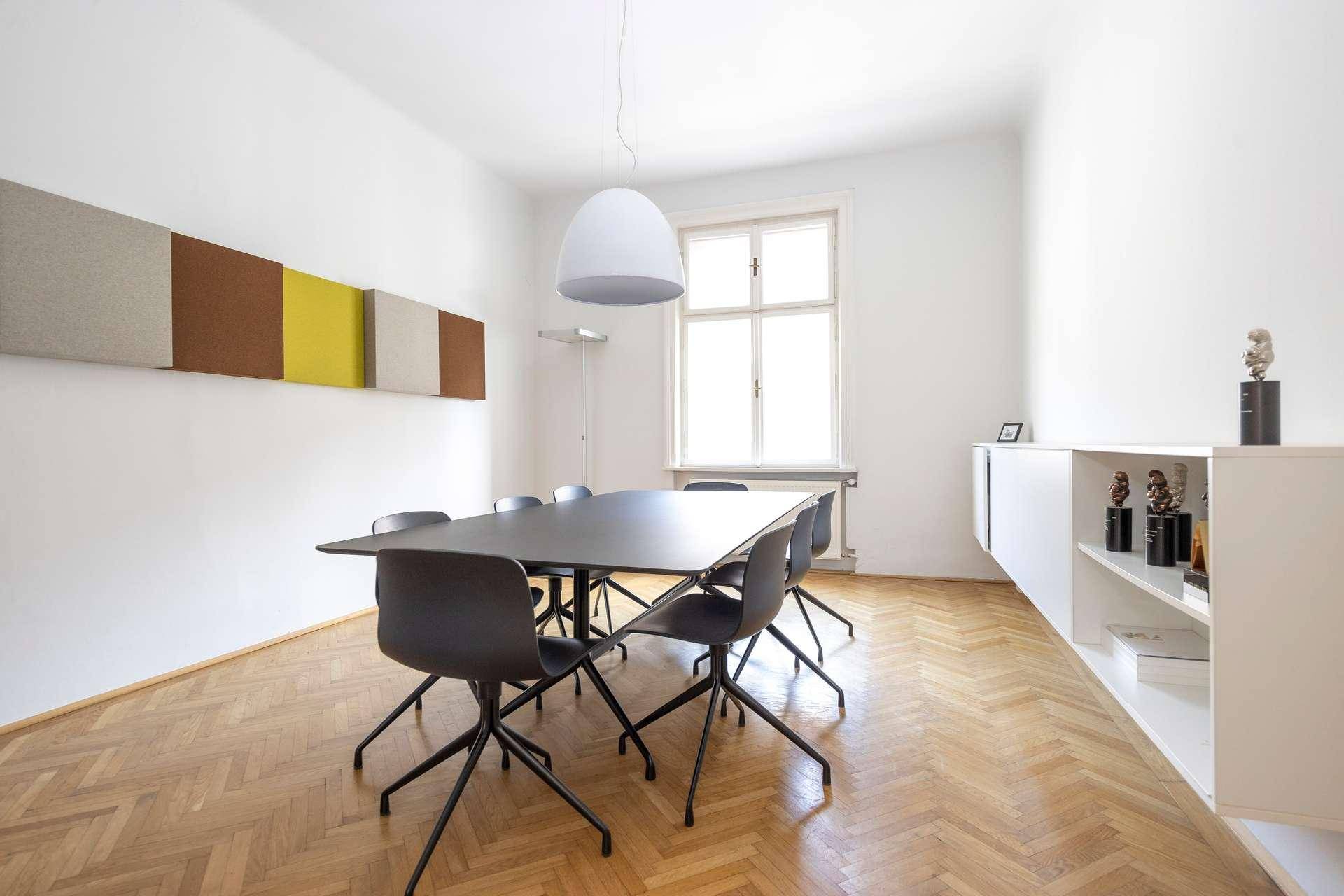 Moderner Konferenzraum mit großem schwarzen Tisch, Designerstühlen und Fischgrätparkettboden unter einem Pendelleuchte.