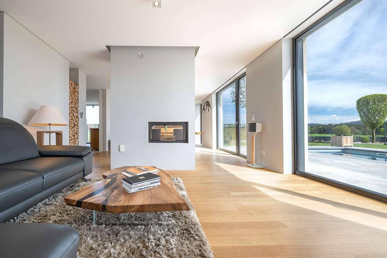 Stilvolles Wohnzimmer mit Ledersofa, Holztisch und Kamin, umgeben von großen Fenstern.