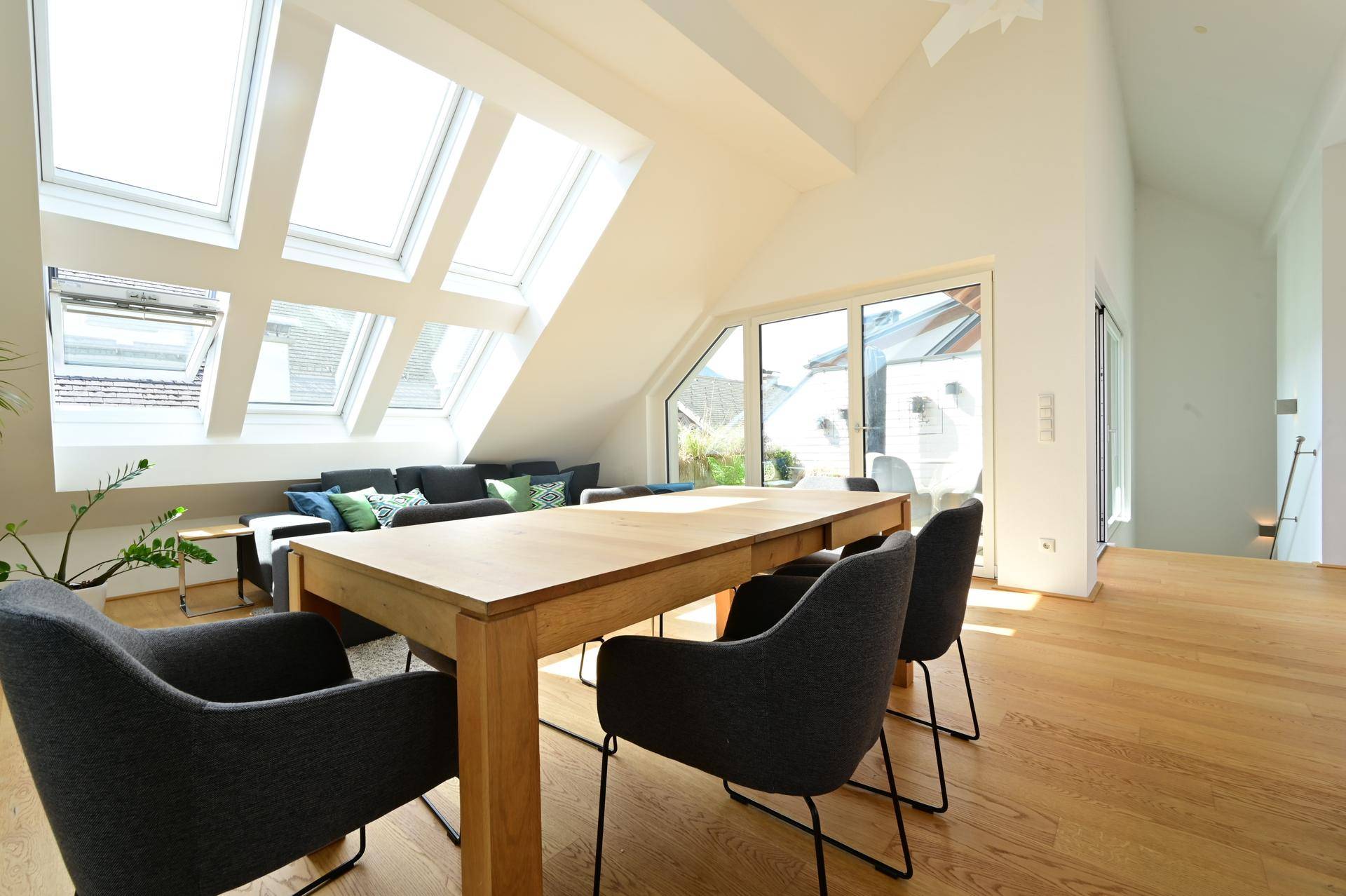 Lichtdurchfluteter Wohn-Essbereich mit Holztisch, bequemen Stühlen und Zugang zur Terrasse durch große Fenster.