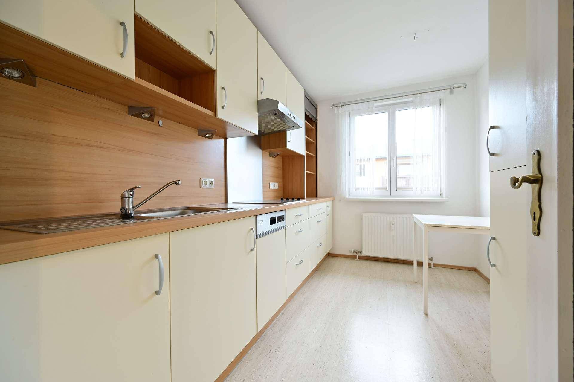 Funktionale Küche mit hellen Schränken, Holzarbeitsplatte und Fenster, inklusive Geschirrspüler.