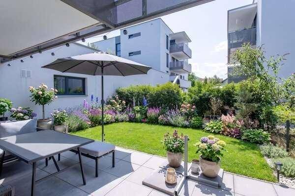 Gepflegter Garten mit Terrasse, Rasenfläche und bunten Blumenbeeten.