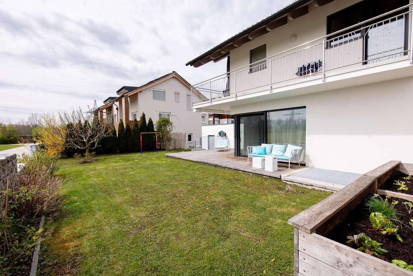 Gartenbereich mit Holzterrasse, Rasen und Hochbeet, ideal für Entspannung im Freien.