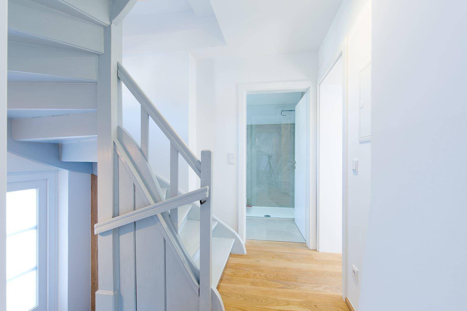 Heller Flur mit Holztreppe und Blick auf ein modernes Badezimmer mit Dusche.
