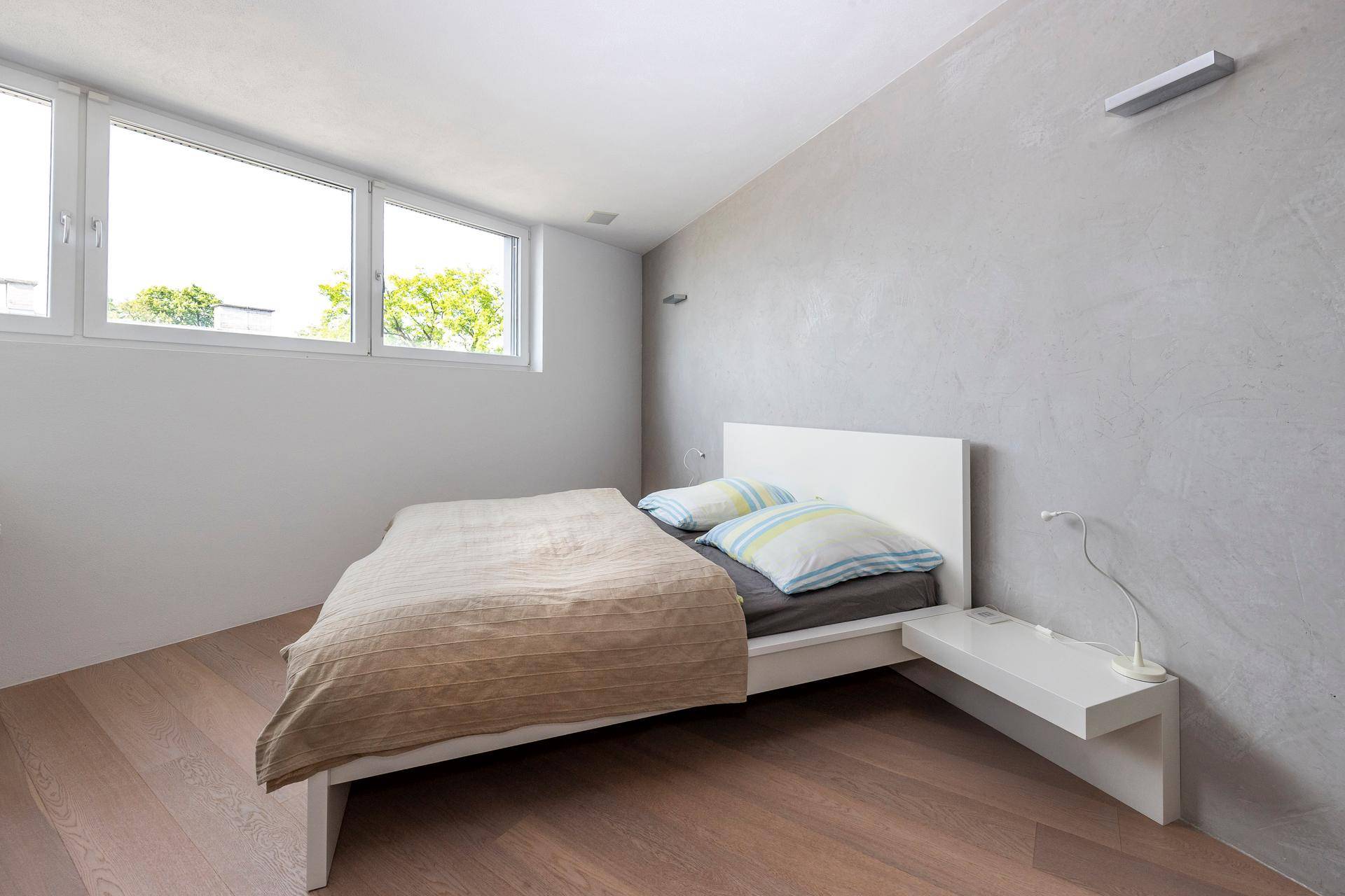 Helles Schlafzimmer mit modernem Bett, Holzboden und großen Fenstern für viel Licht.