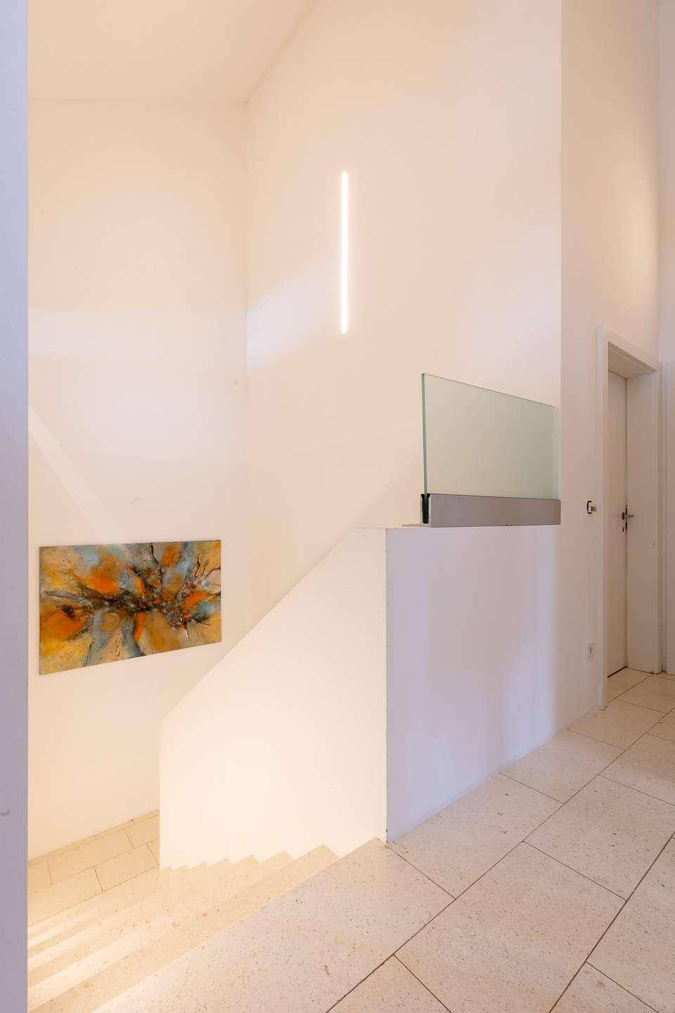 Heller Treppenaufgang mit moderner Beleuchtung und Kunst an der Wand.