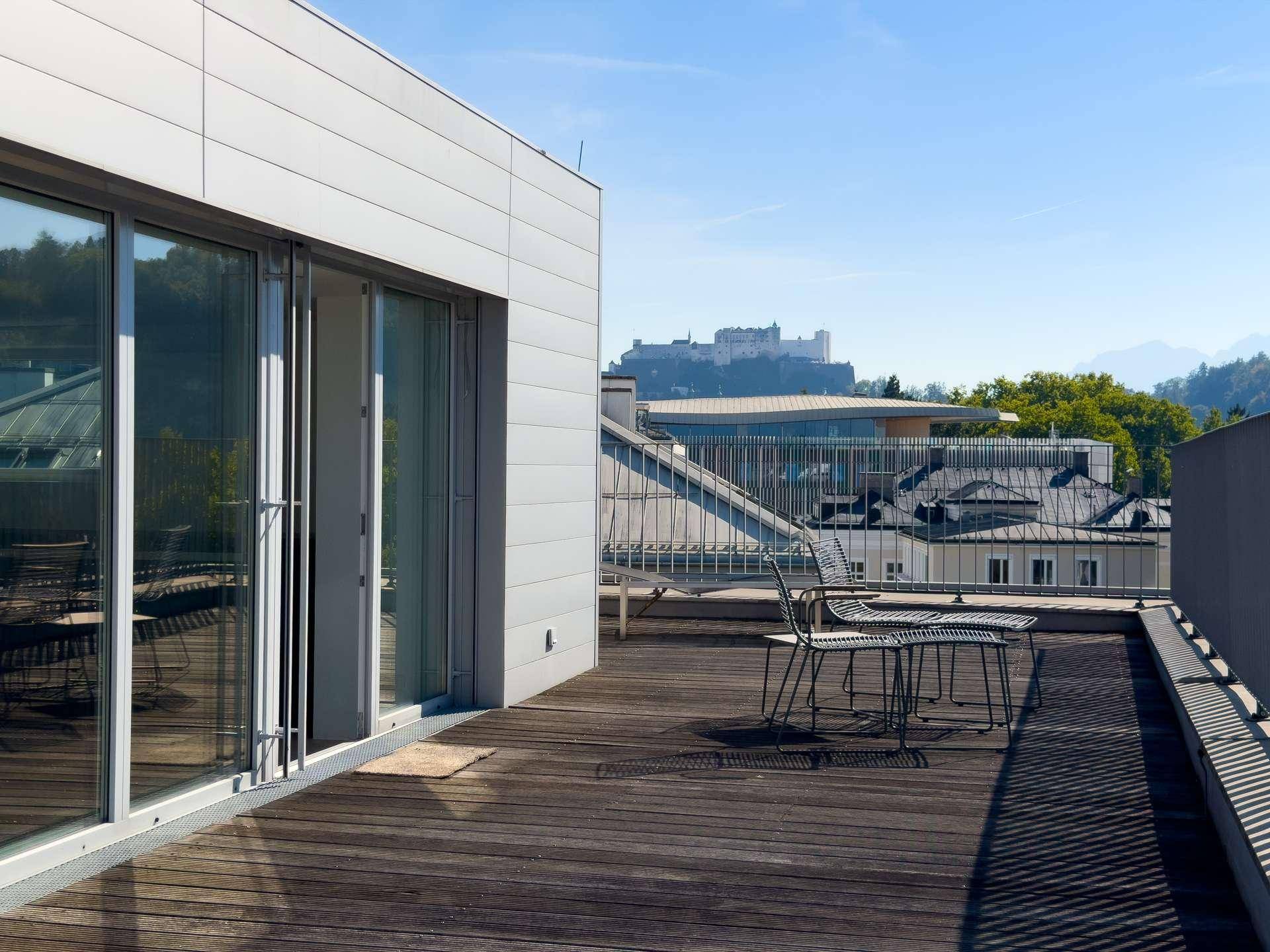 Geräumige Dachterrasse mit Holzboden, Sitzgelegenheiten und Fernblick auf die Stadt und Berge.