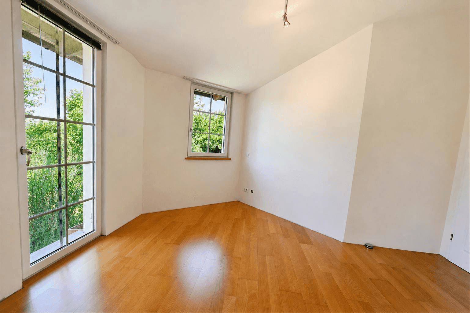 Helles Schlafzimmer mit Holzboden und großen Fenstern, die viel Tageslicht hereinlassen.