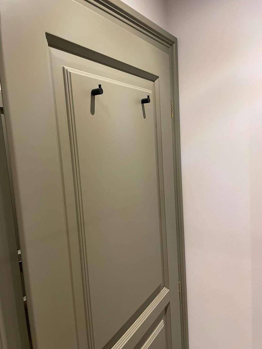 Detailansicht einer hellgrauen Tür mit dekorativen schwarzen Haken.