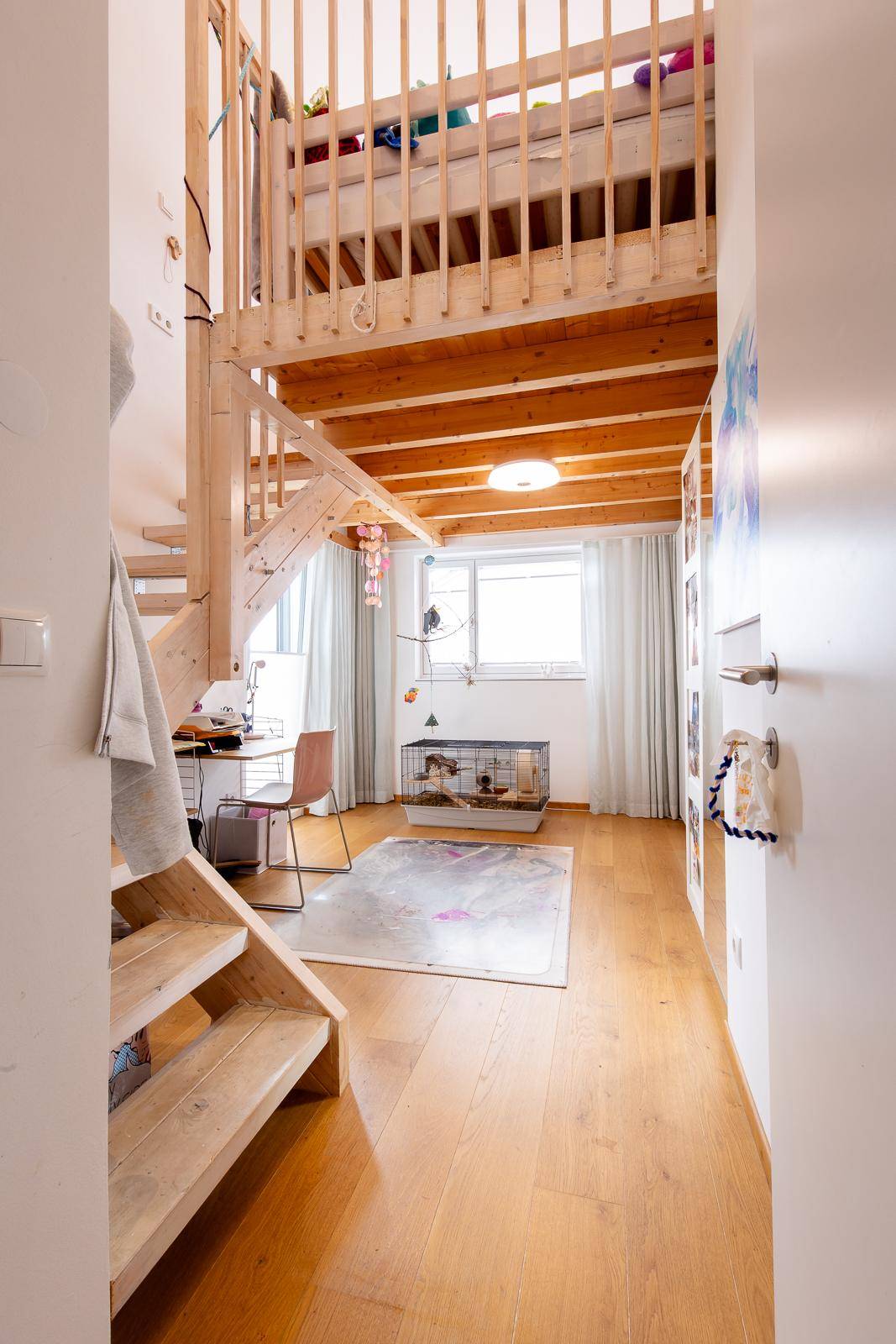 Kinderzimmer mit Holzboden, Hochbett und einem Arbeitsbereich unter dem Fenster.