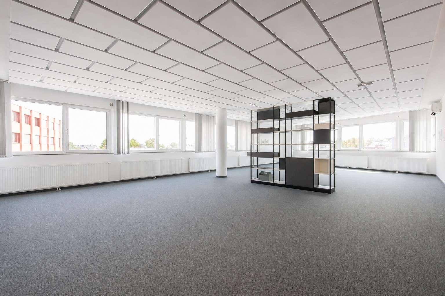 Helles, offenes Büro mit vielen Fenstern, Teppichboden und einem modernen Raumteiler.
