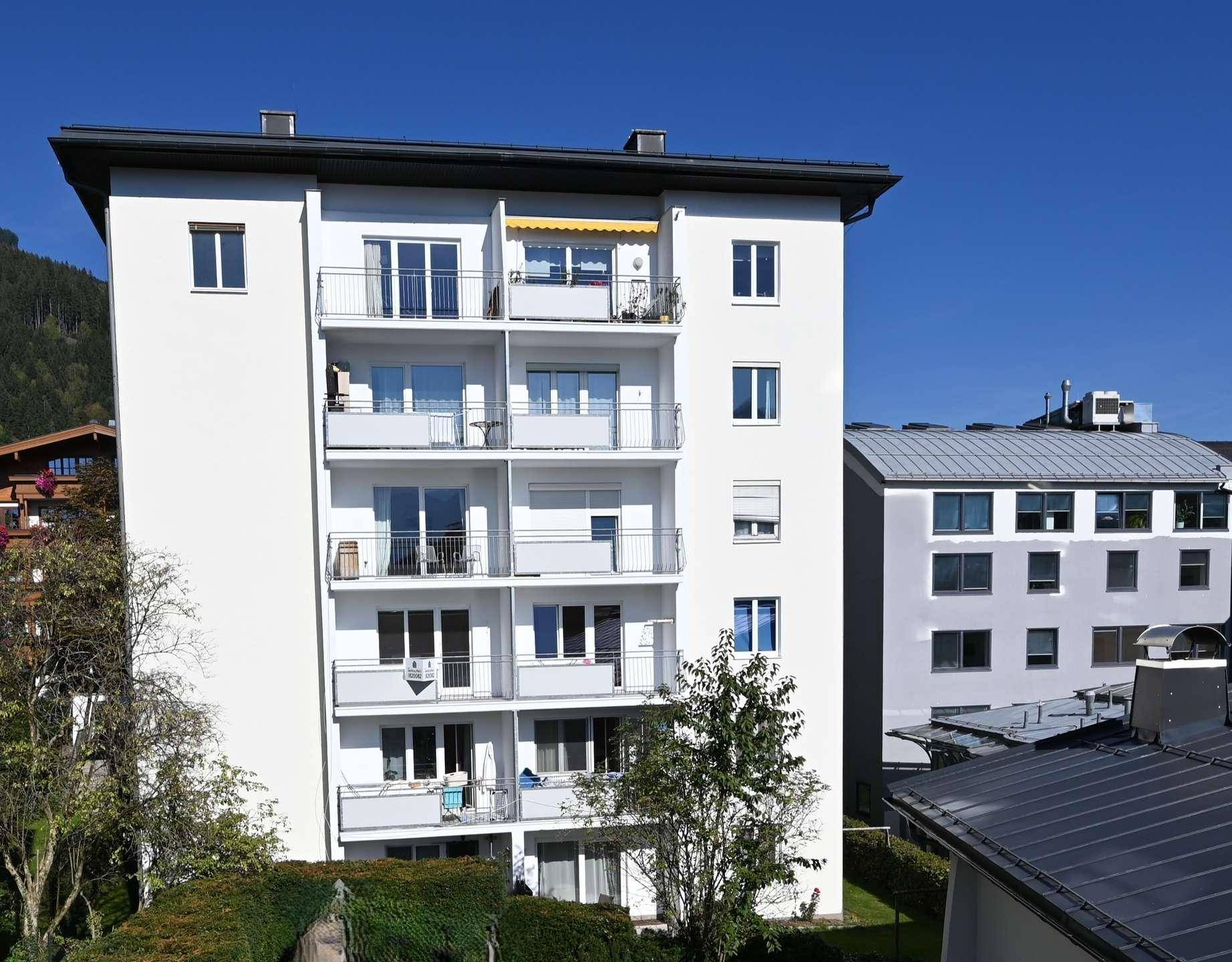 Modernes Mehrfamilienhaus mit mehreren Balkonen und einer hellen Fassade unter blauem Himmel.