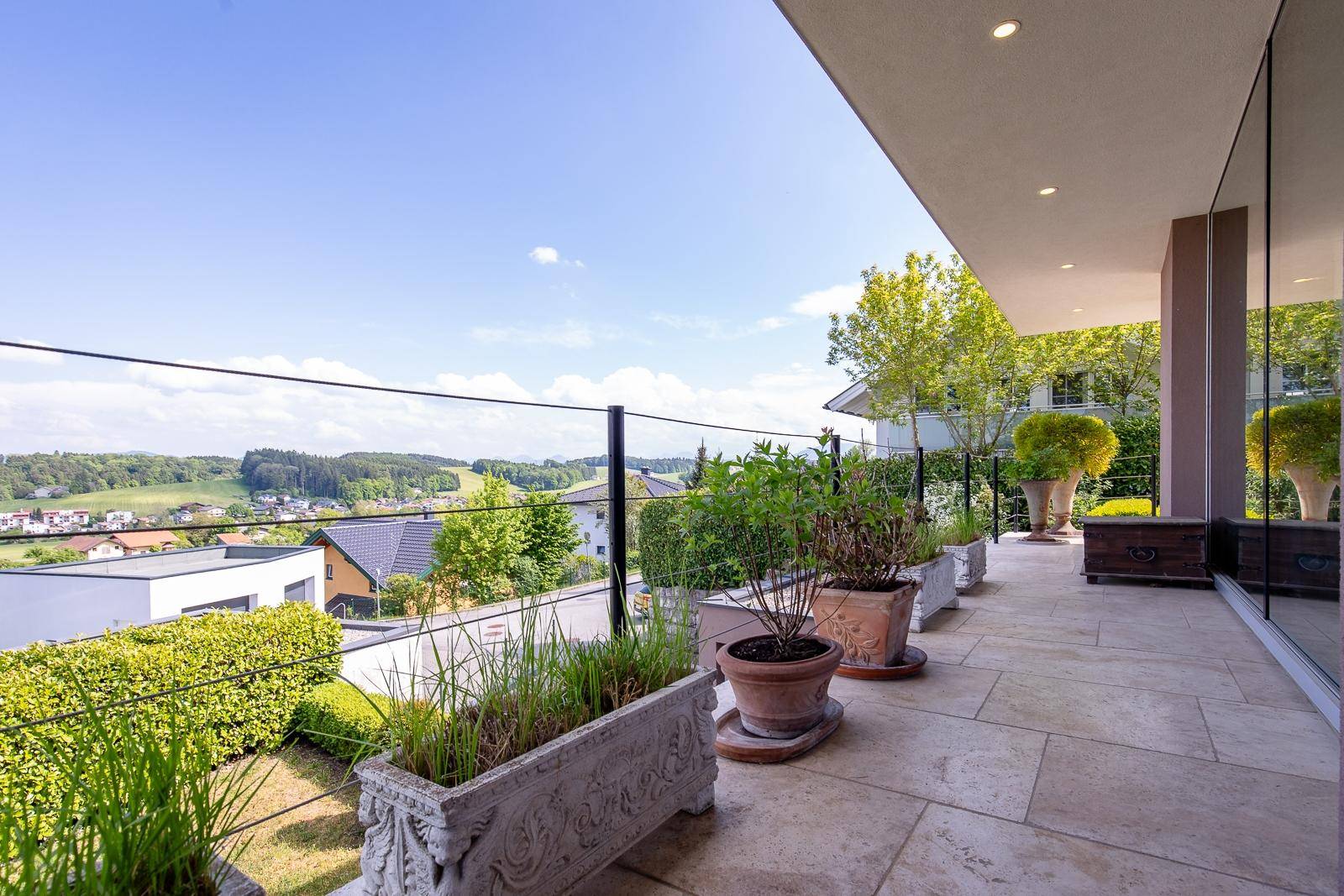 Langer Balkon mit Pflanzenkübeln und weitem Blick über die grüne Landschaft.